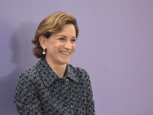 Anne Applebaum trägt eine gemusterte Bluse, steht vor einem violetten Hintergrund und schaut an der Kamera vorbei