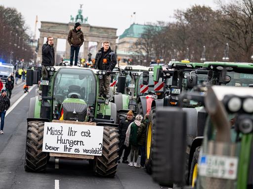 Viele Traktoren stehen vor dem Brandenburger Tor; Landwirte streiken gegen die Pläne der Bundesregierung; an einem Traktor hängt ein Transparent mit der Aufschrift "Müsst ihr erst Hungern bevor ihr es versteht?" (18.12.20223)