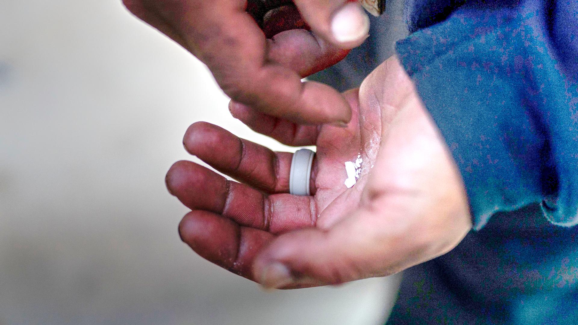 Eine obdachlose Person hält zerbröselte Fentanyl-Tabletten in der Hand. Nahaufnahme der Hände.