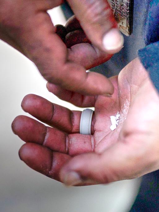 Eine obdachlose Person hält zerbröselte Fentanyl-Tabletten in der Hand. Nahaufnahme der Hände.