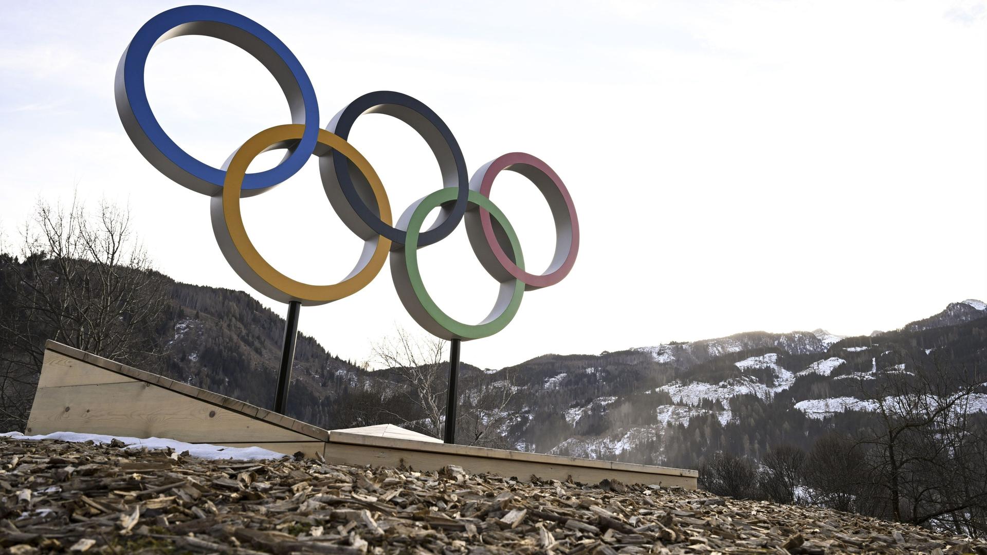 Die Olympischen Ringe stehen vor einer nahezu schneefreien Berglandschaft. Die Olympischen Ringe stehen vor einer nahezu schneefreien Berglandschaft.