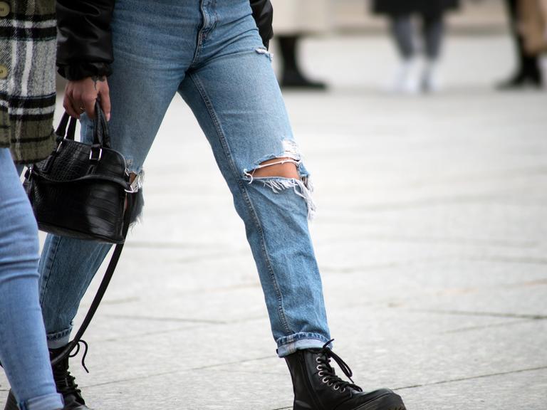 Zwei junge Frauen mit Handtasche und löchriger Jeans gehen über einen Platz. Zwei junge Frauen mit Handtasche und löchriger Jeans gehen über einen Platz.
