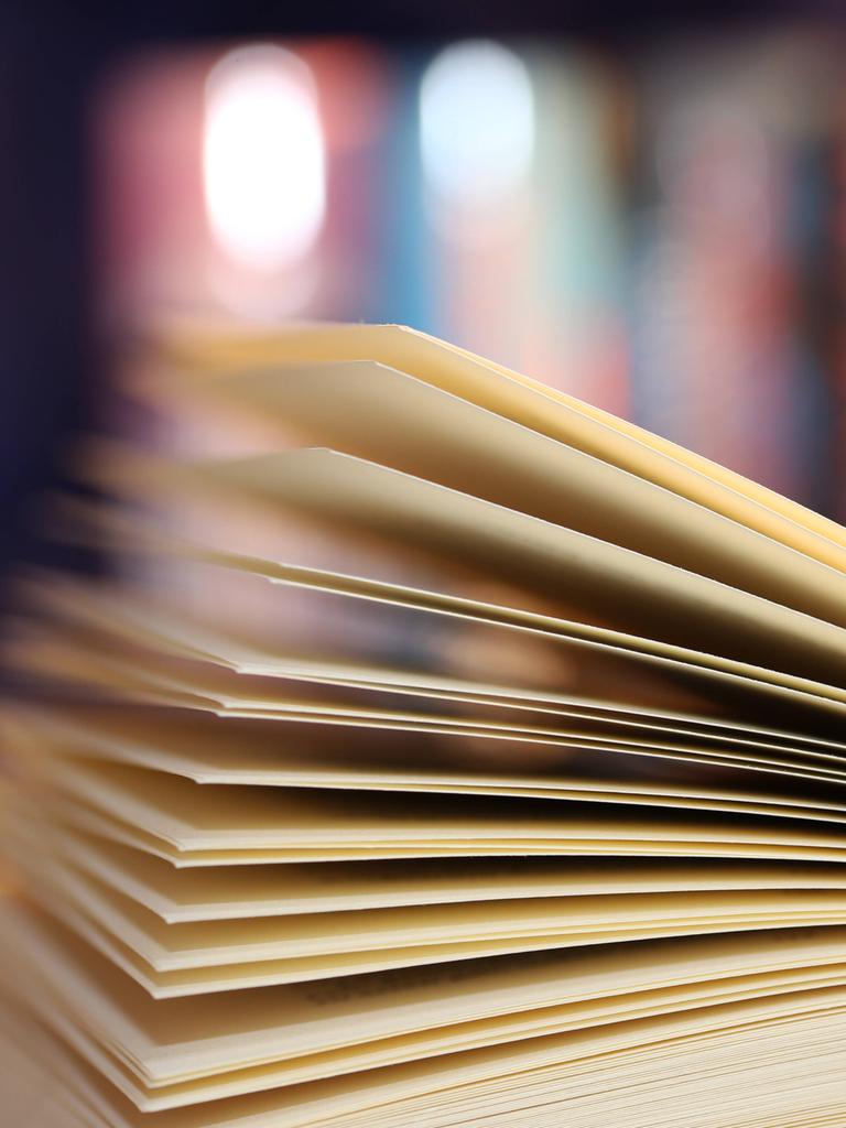Ein aufgeschlagenes Buch. Sehr unscharf im Hintergrund stehen weitere Bücher in einem Regal.