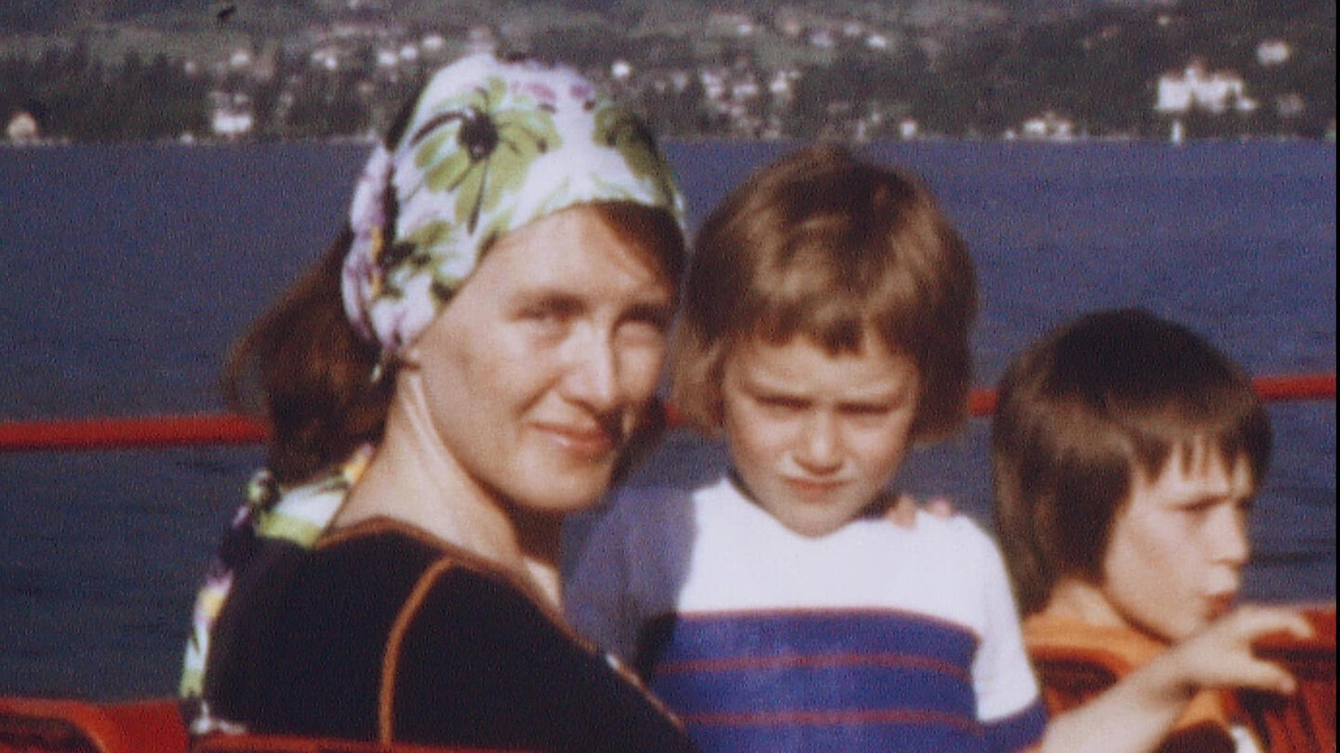 Alte Aufnahme von Annie Ernaux, die als junge Frau ein geblümtes Kopftuch trägt und mit zwei Kindern auf dem Oberdeck eines Ausflugsdampfers sitzt.