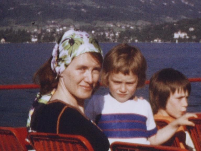 Alte Aufnahme von Annie Ernaux, die als junge Frau ein geblümtes Kopftuch trägt und mit zwei Kindern auf dem Oberdeck eines Ausflugsdampfers sitzt.