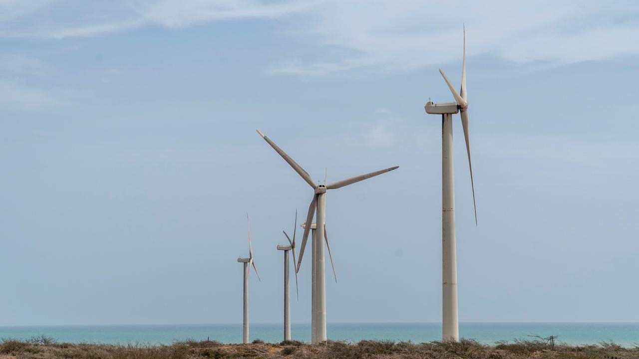 Windräder stehen an der Küste, im Hintergrund ist das Meer zu sehen.