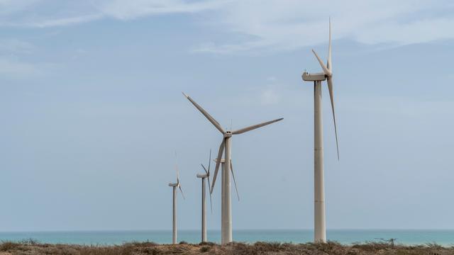 Windräder stehen an der Küste, im Hintergrund ist das Meer zu sehen.