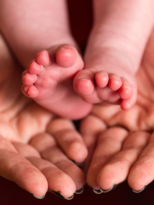Die nackten Füße eines Babys in den Händen einer Frau Die nackten Füße eines Babys in den Händen einer Frau