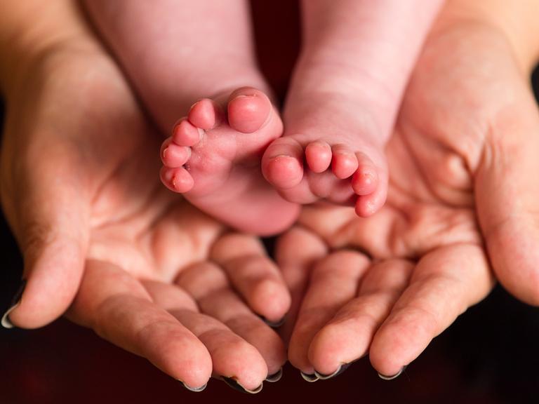 Die nackten Füße eines Babys in den Händen einer Frau Die nackten Füße eines Babys in den Händen einer Frau