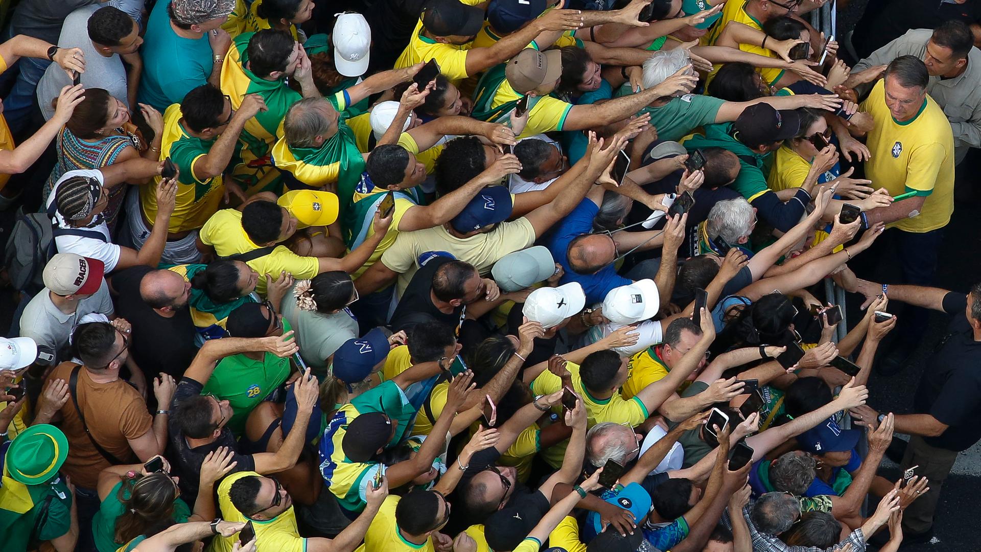 Viele Menschen in den brasilianischen Nationalfarben Gelb und Grün stehen dicht gedrängt. Am oberen rechten Bildrand steht Jair Bolsonaro. 