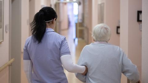 Eine Pflegefachkraft geht mit einer Bewohnerin einer Einrichtung über einen Gang