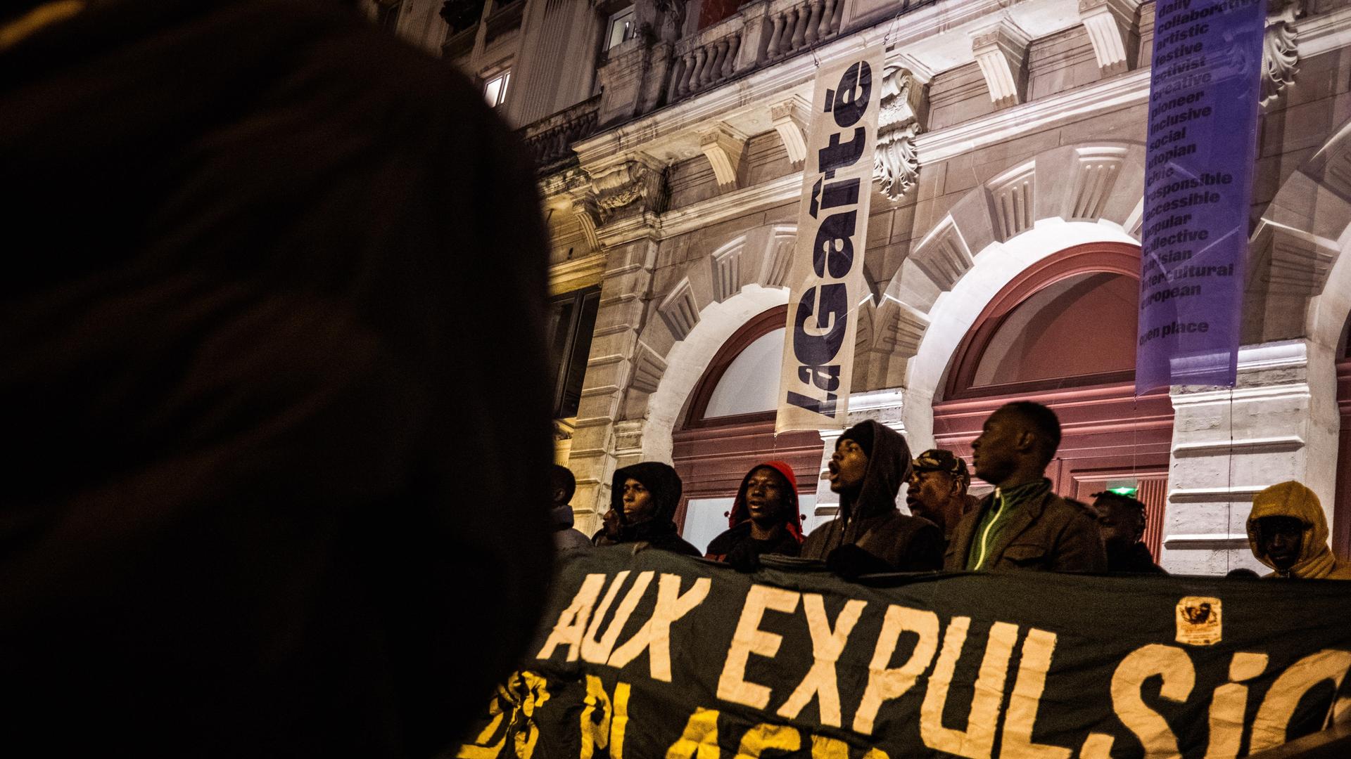 Afrikanische Migranten stehen vor dem Theater und halten Banner vor sich.