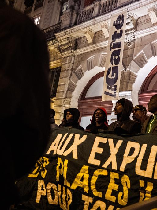 Afrikanische Migranten stehen vor dem Theater und halten Banner vor sich.