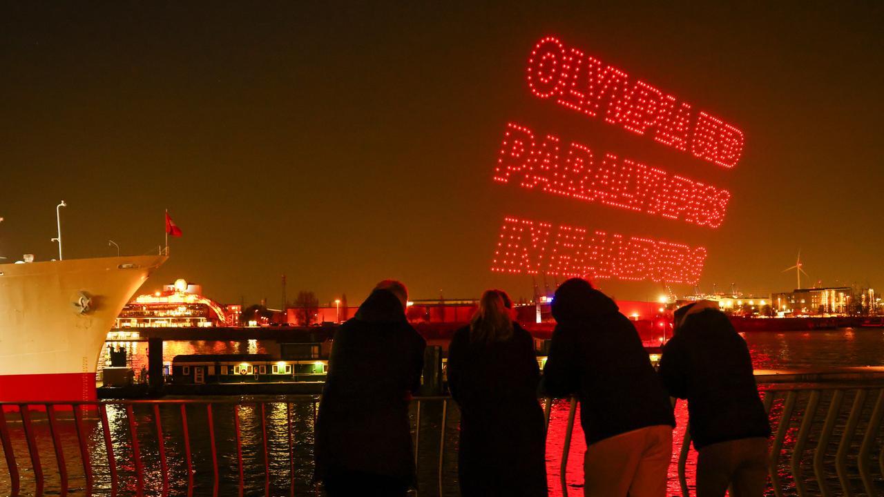 Drohnen bilden den Slogan "Olympia und Paralympics in Hamburg" am dunklen Himmel über der Elbe an den Landungsbrücken.