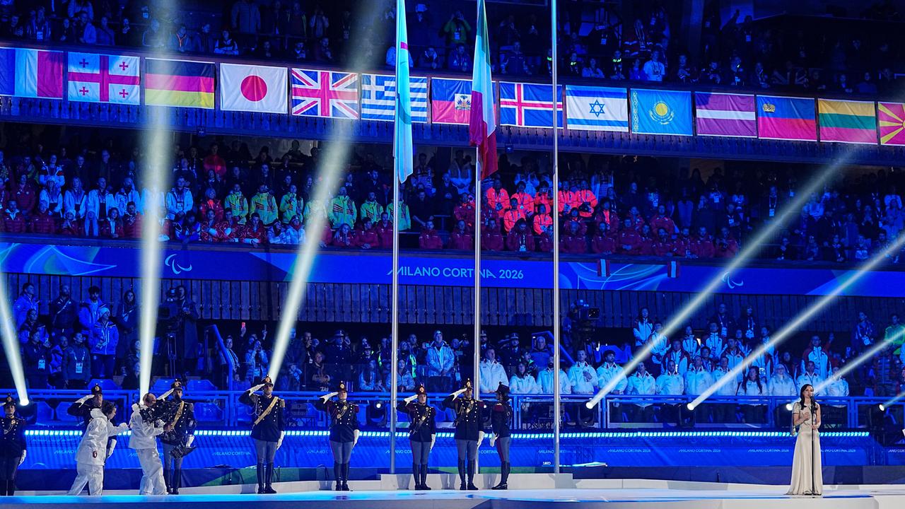 Die Abschlussfeier der Paralympischen Winterspiele in Cortina. Das Stadion ist in blaues Licht getaucht. Zu sehen sind die Fahnen der Nationen und Laserstrahlen.