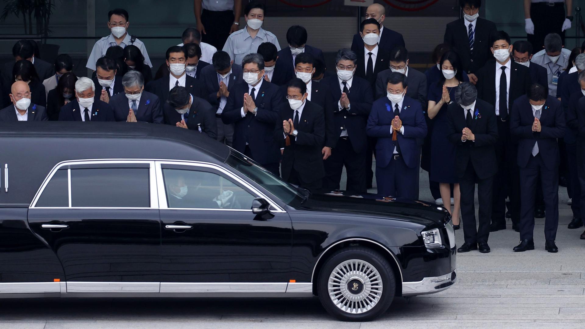 Ein großes schwarzes Auto mit dem verstorbenen Shinzo Abe fährt an Freunden und Verwandten vorbei, die die Hände gefaltet haben und sich verneigen. Foto: picture alliance