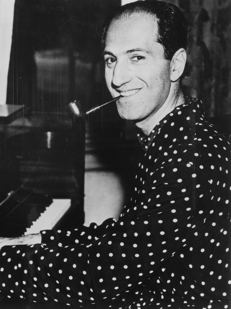 Ein Schwarzweiß-Foto zeigt den Komponisten George Gershwin am Flügel sitzend und in die Kamera lächelnd.