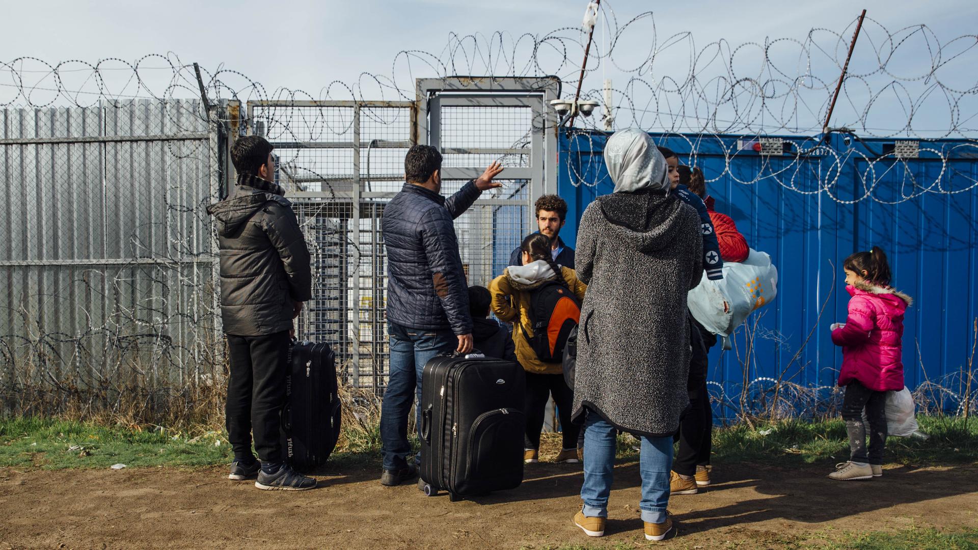 Eine syrische Flüchtlingsfamilie an der geschlossenen Balkanroute im Jahr 2017 steht vor einem geschlossenen Zaun mit Stacheldraht an der Grenze von Ungarn. Eine syrische Flüchtlingsfamilie an der geschlossenen Balkanroute im Jahr 2017 steht vor einem geschlossenen Zaun mit Stacheldraht an der Grenze von Ungarn.
