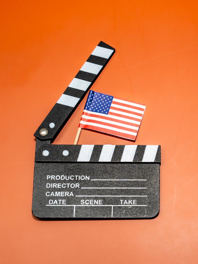 Auf einem leuchtend orangefarbenen Hintergrund ist eine Filmklappe mit einer amerikanischen Flagge zu sehen, die für das Filmemachen und patriotische Themen steht.