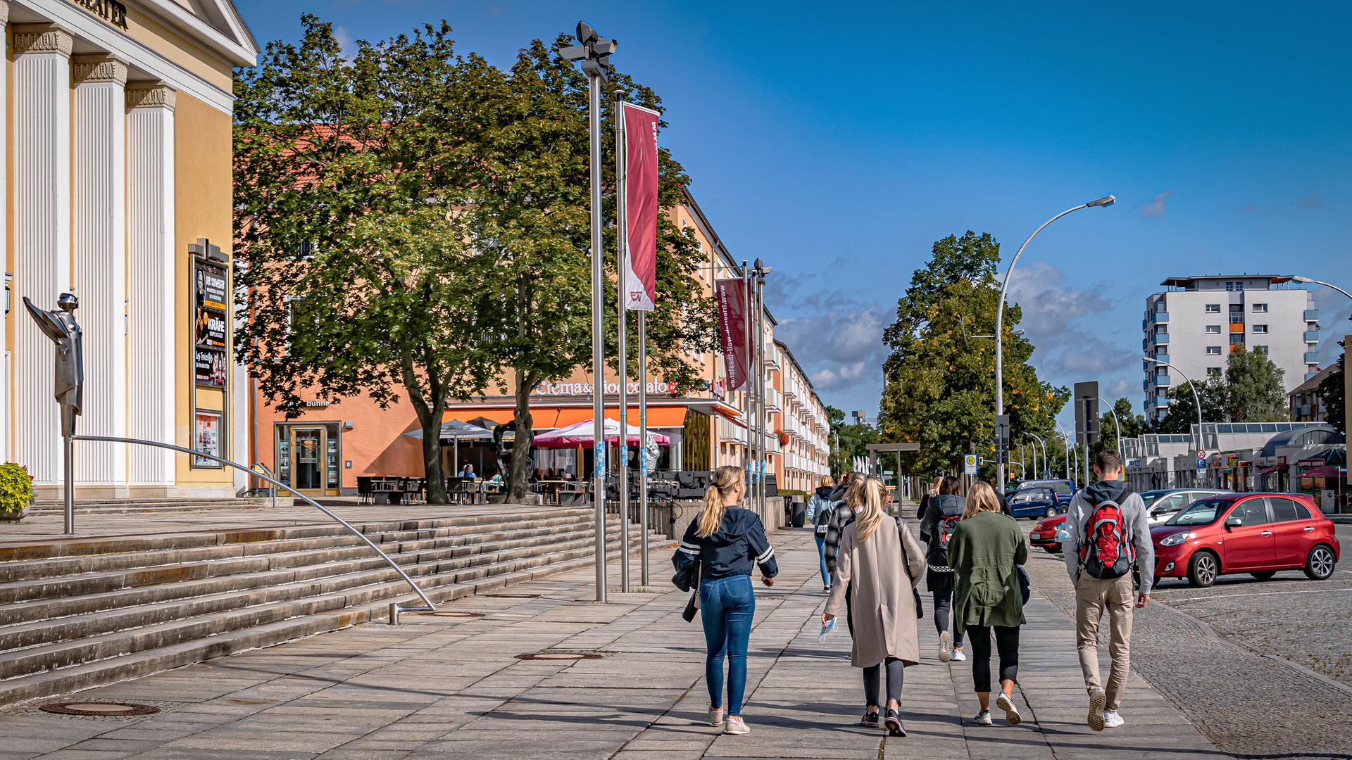 Passanten gehen an einem sonnigen Tag am Friedrich Wolf Theater in Eisenhüttenstadt vorbei.