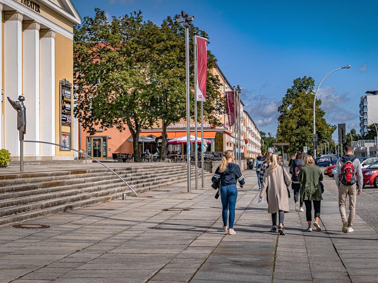 Passanten gehen an einem sonnigen Tag am Friedrich Wolf Theater in Eisenhüttenstadt vorbei.