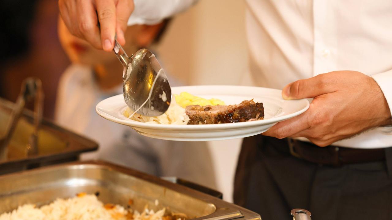 Ein junger Mann legt Garnierung zum Fleisch auf seinen Teller. 
