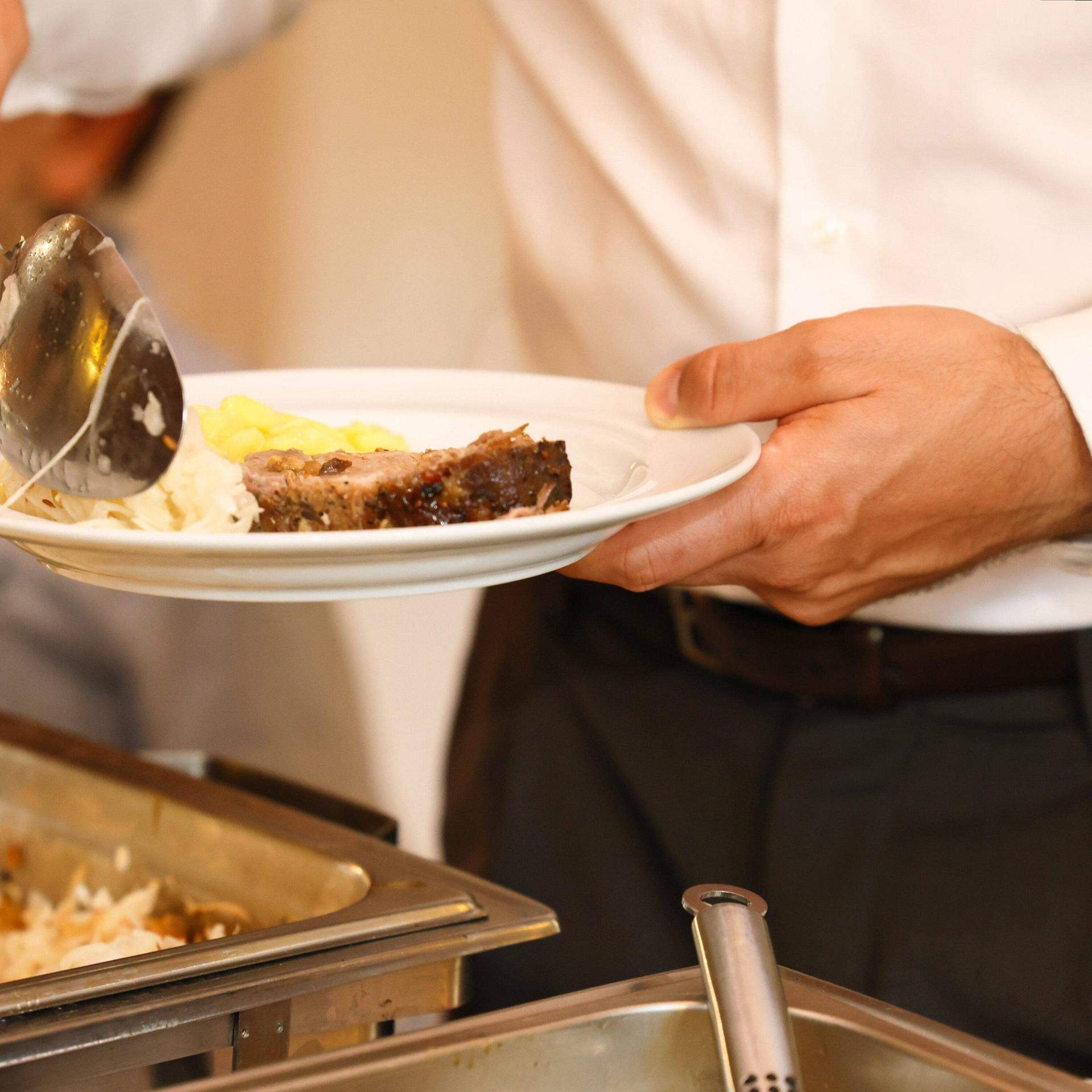Ein junger Mann legt Garnierung zum Fleisch auf seinen Teller. 