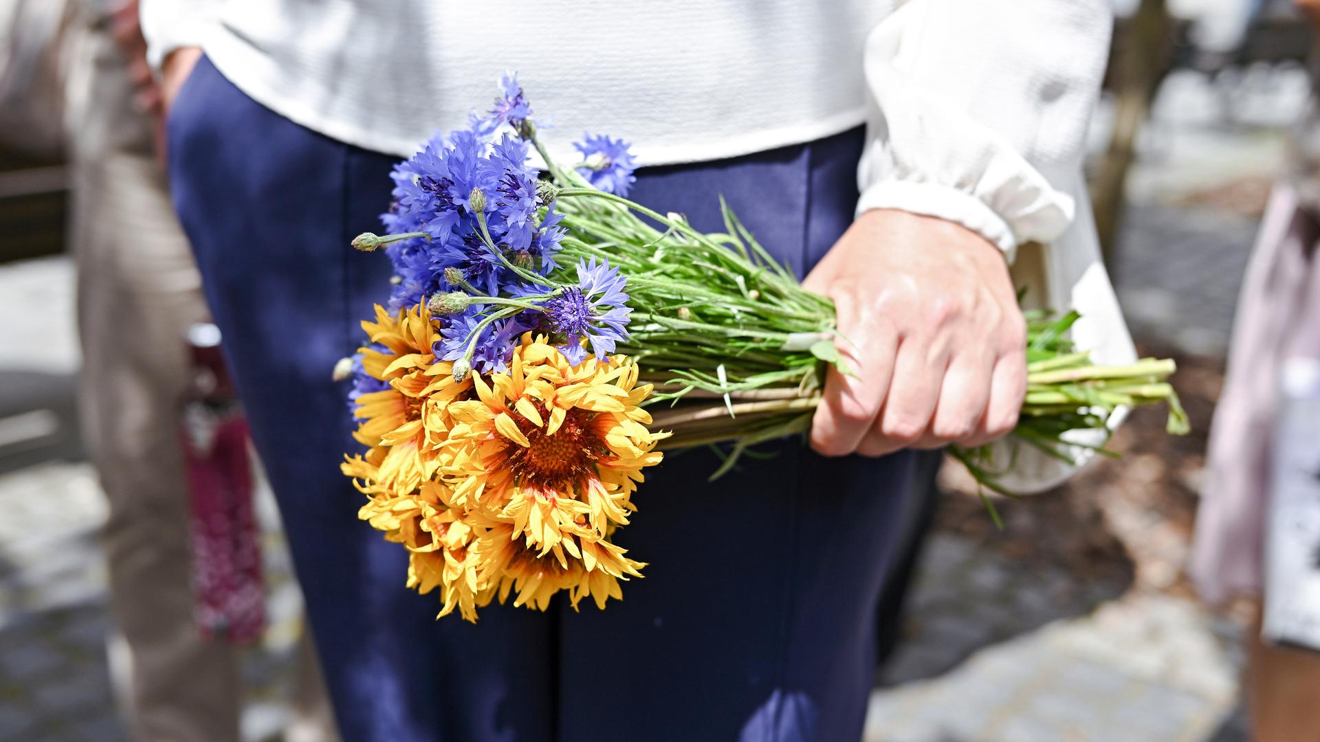 Die Hände einer Frau halten einen Strauß aus Blumen in den ukrainischen Farben gelb und blau.