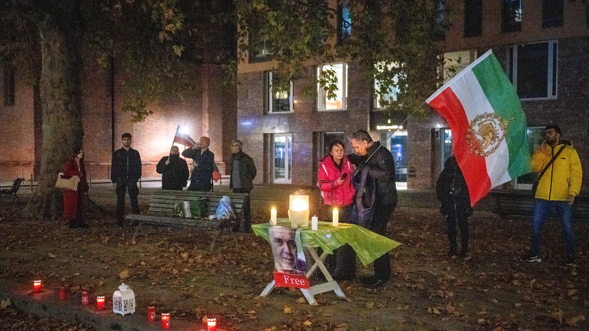 Eine Kundgebung vor dem Auswärtigen Amt für den Deutsch-Iraner Djamshid Sharmahd, mit Fahne und Lichtern am Abend. 