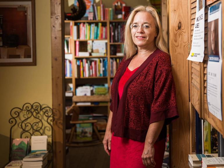 Die Dresdner Buchhändlerin Susanne Dagen im roten Kleid mit Jacke. Sie steht vor einer Bücherwand. 