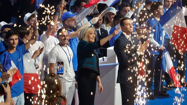 Marine Le Pen und ihr Parteichef Bardella vom Rassemblement National stehen auf einer Bühne, umringt von Anhängern, und feiern.