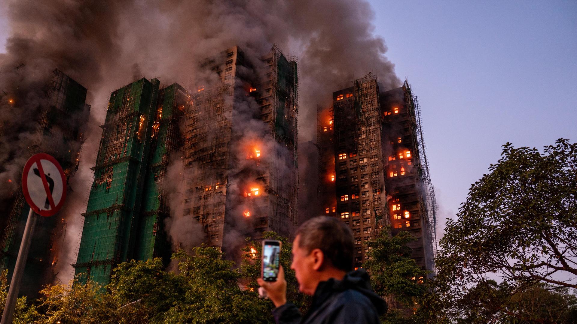 Ein Mann nimmt mit seinem Handy Rauch und Flammen auf, als ein Großbrand mehrere Wohngebäude in Hongkong erfasst.