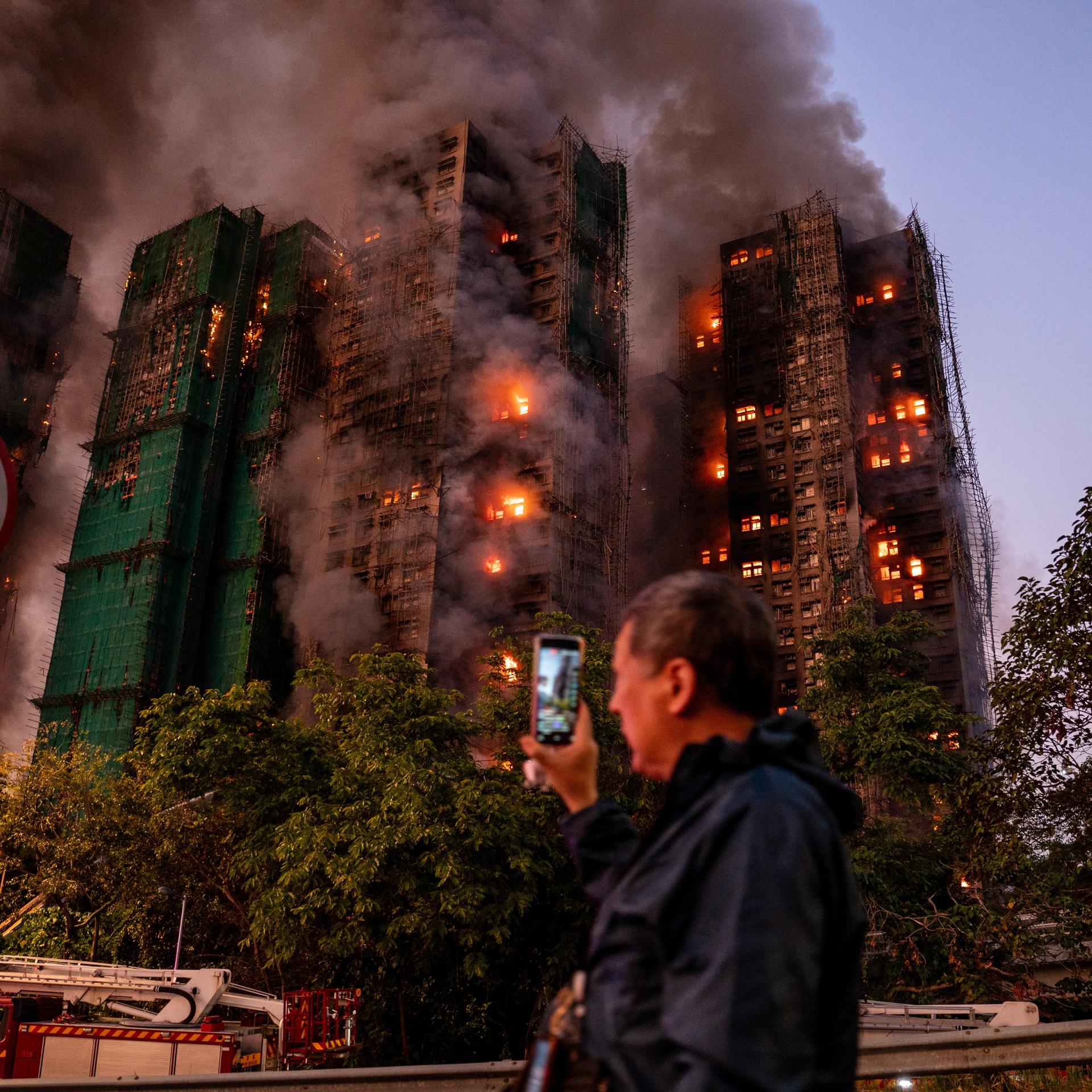 Ein Mann nimmt mit seinem Handy Rauch und Flammen auf, als ein Großbrand mehrere Wohngebäude im Wang Fuk Court in Hongkong erfasst.