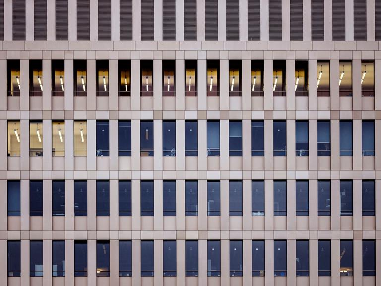 Blick von außen auf die hellbraune Fassade des Bundesnachrichtendienstes in Berlin. Mehrere Fensterreihen, in wenigen Fenstern brennt Licht. Es ist tags.