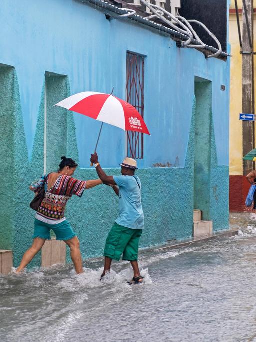 Kubaner mit Regenschirmen auf einer überfluteten Straße bei sintflutartigem Regen in der Stadt Santiago de Cuba auf der Insel Kuba.