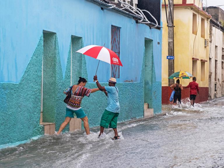 Kubaner mit Regenschirmen auf einer überfluteten Straße bei sintflutartigem Regen in der Stadt Santiago de Cuba auf der Insel Kuba.
