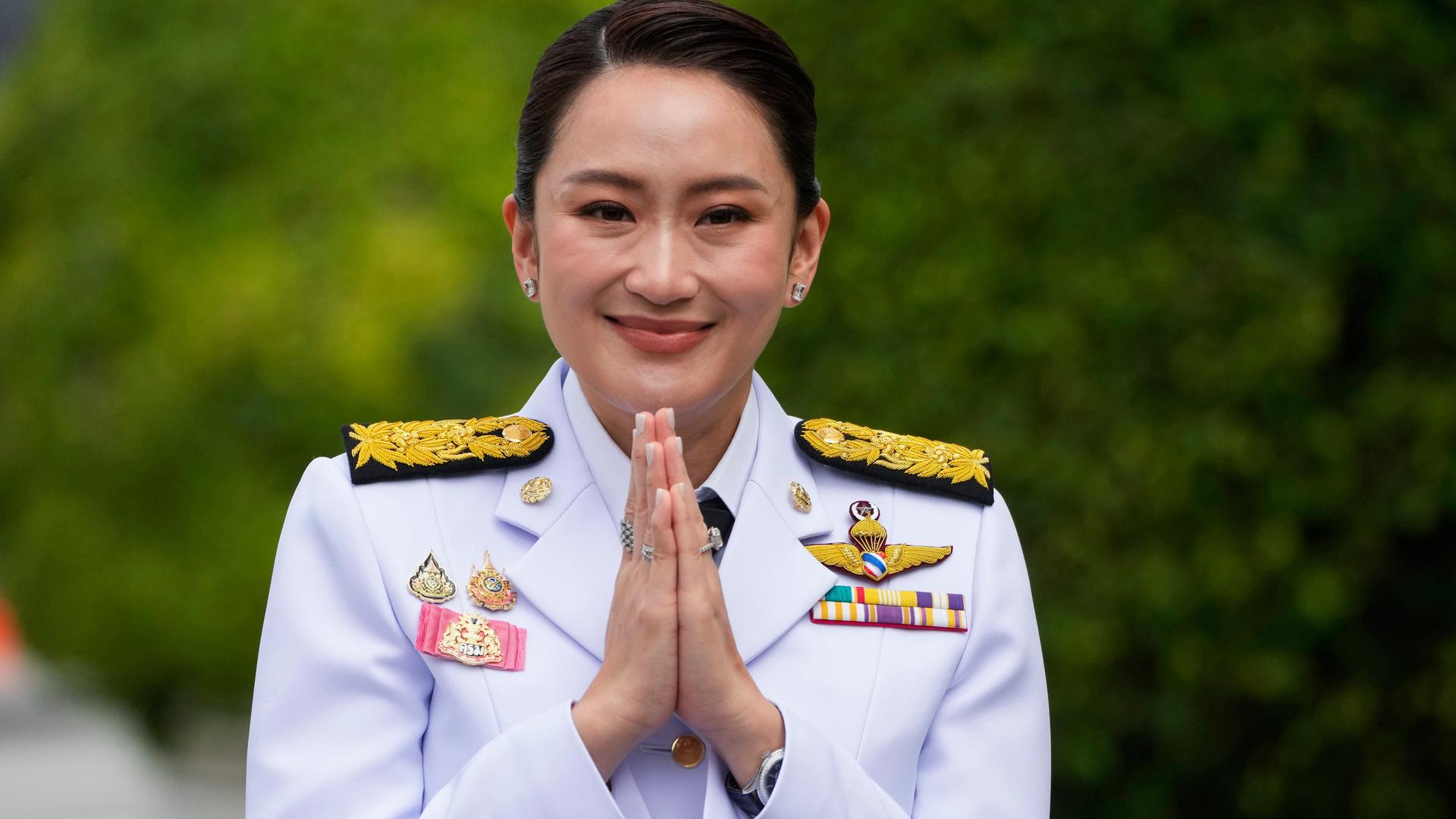 Thailands neue Premierministerin Paetongtarn Shinawatra lächelt in weißer Uniform mit verschiedenen Abzeichen und gefalteten Händen in die Kamera.