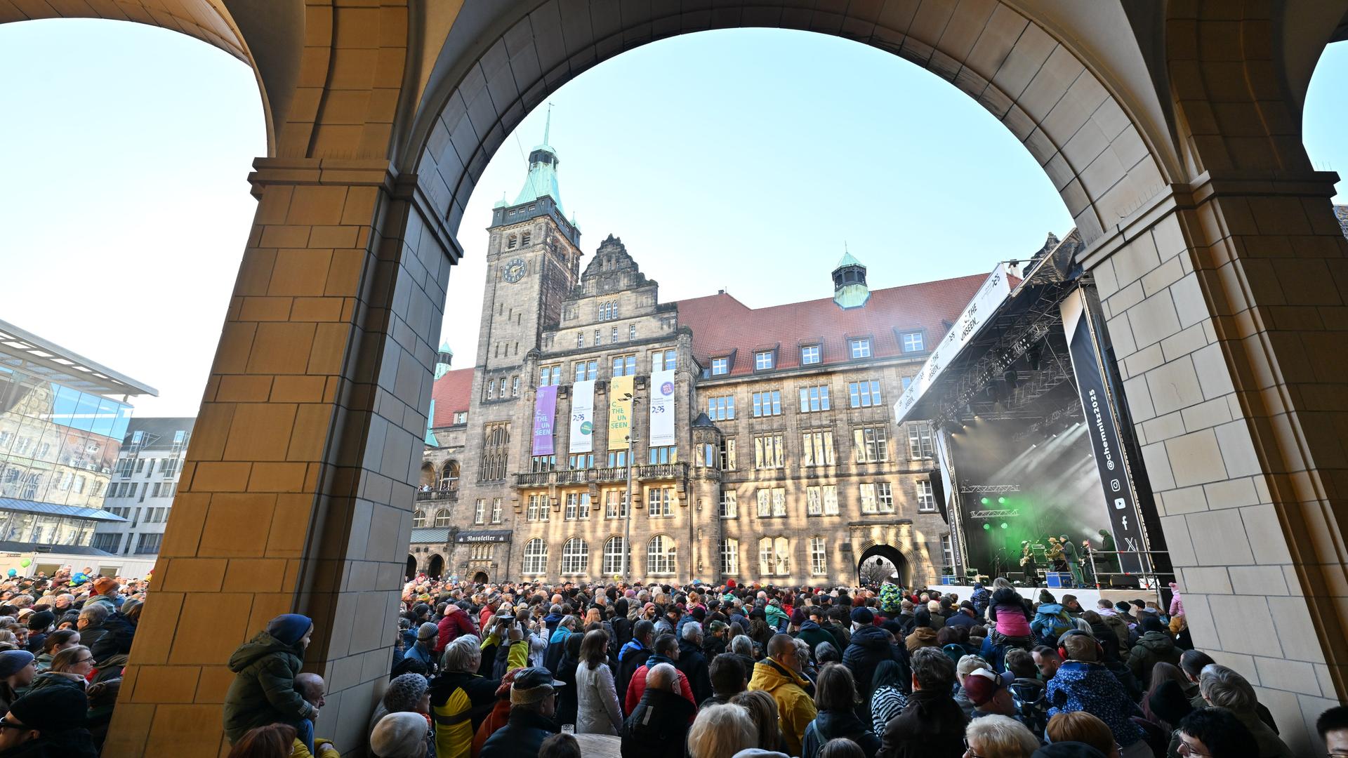 Das Gundermann Ensemble, Alexander Scheer und Andreas Dresen & Band spielen zum Start in das Jahr als Europäische Kulturhauptstadt in Chemnitz auf dem Neumarkt vor dem Rathaus. Man sieht zahlreiche Menschen auf dem Platz.