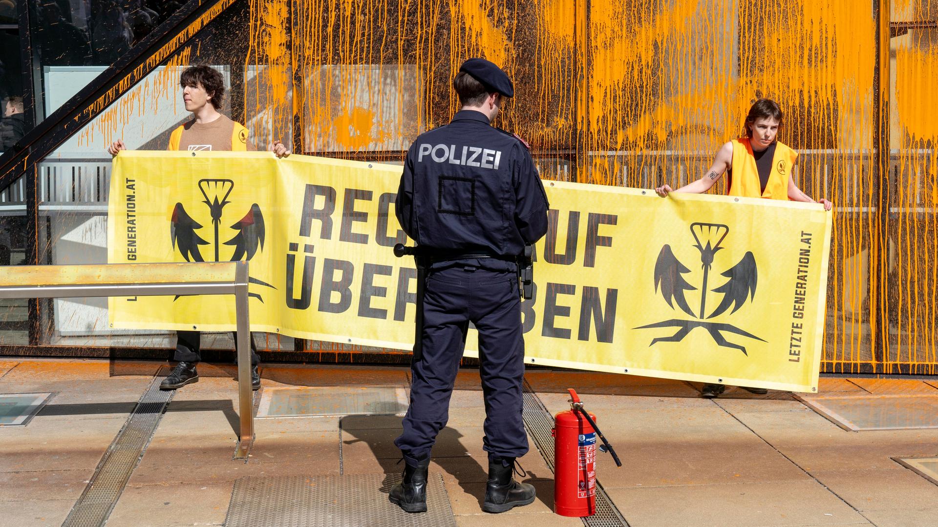 Klimaaktivisten der "Letzten Generation" protestieren in Wien. Sie halten ein Plakat mit der Aufschrift "Recht auf Überleben". Vor ihnen steht ein Polizist.