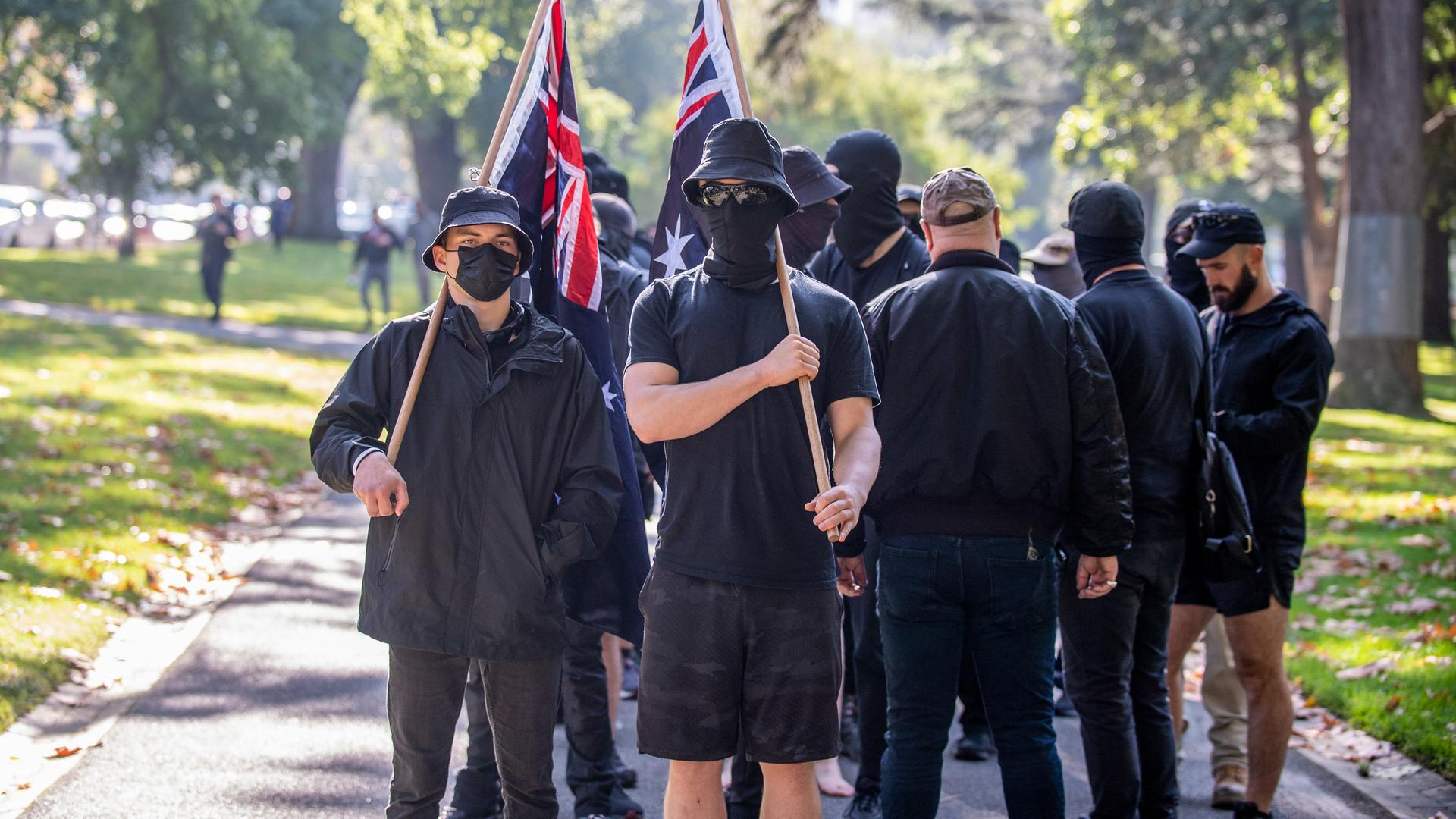 Neonazis in schwarz gekleidet tragen die australische Flagge durch einen Park Neonazis in schwarz gekleidet tragen die australische Flagge durch einen Park