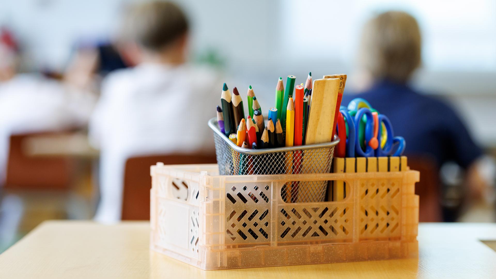 Schüler einer zweiten Klasse einer Grundschule in München (Bayern) sitzen während des Unterrichts auf ihren Plätzen und arbeiten an einer Schulaufgabe, während im Vordergrund ein Kasten mit Stiften, Linealen und Scheren zu sehen ist.