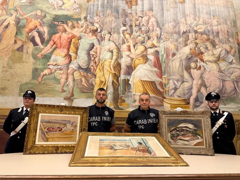 Vier italienische Polizisten posieren mit drei Gemälden von Cezanne, Matisse und Renoir vor einem großen Wandgemälde.