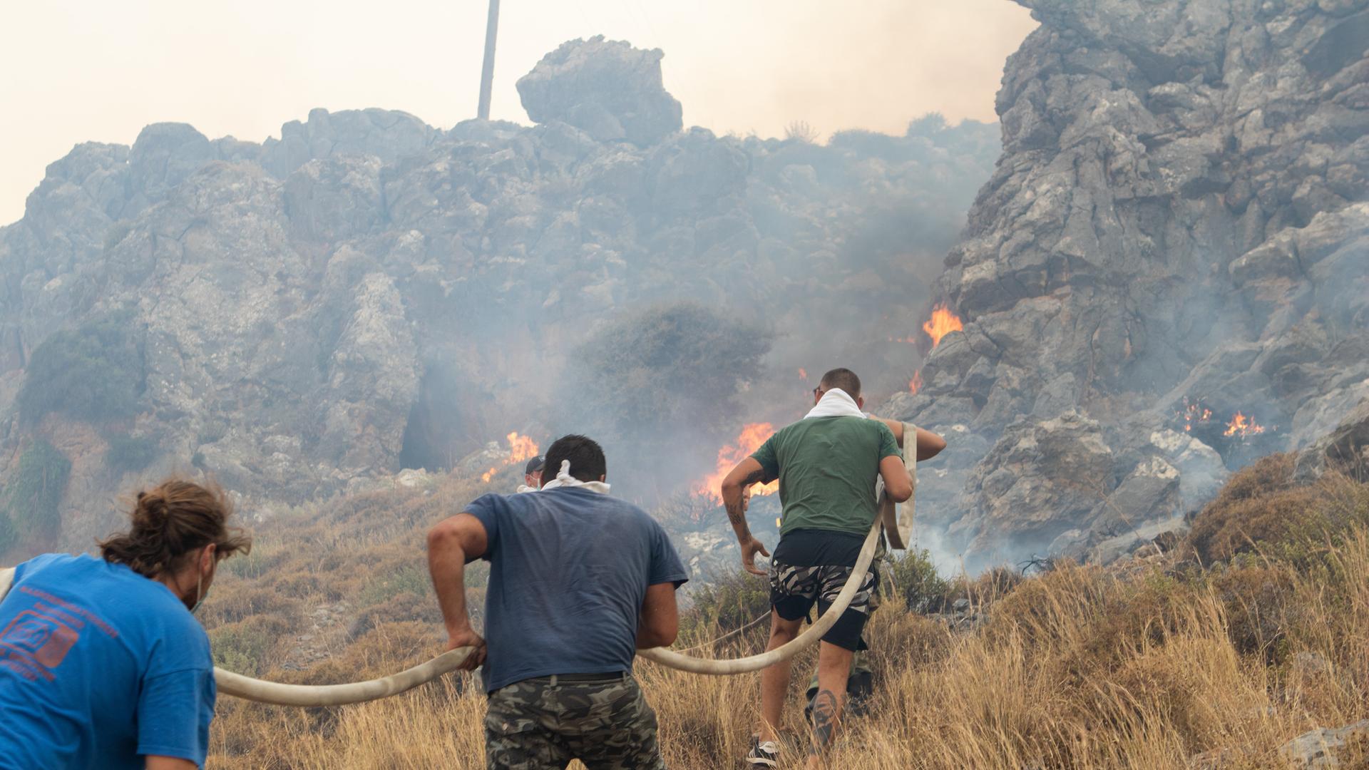 Feuerwehrleute versuchen mit Schläuchen die Waldbrände auf der griechischen Insel Rhodos zu löschen.