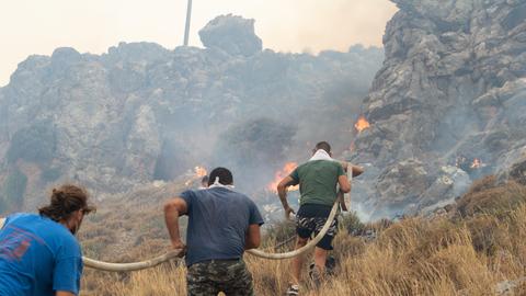 Feuerwehrleute versuchen mit Schläuchen die Waldbrände auf der griechischen Insel Rhodos zu löschen.