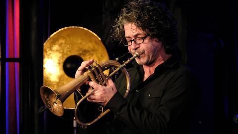Konzert Christoph spielt auf einer Bühne mit goldener Dekoration auf seinem Flügelhorn, das einer großen Trompete ähnelt.