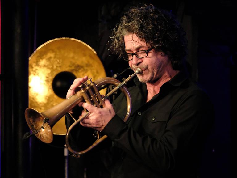 Konzert Christoph spielt auf einer Bühne mit goldener Dekoration auf seinem Flügelhorn, das einer großen Trompete ähnelt.