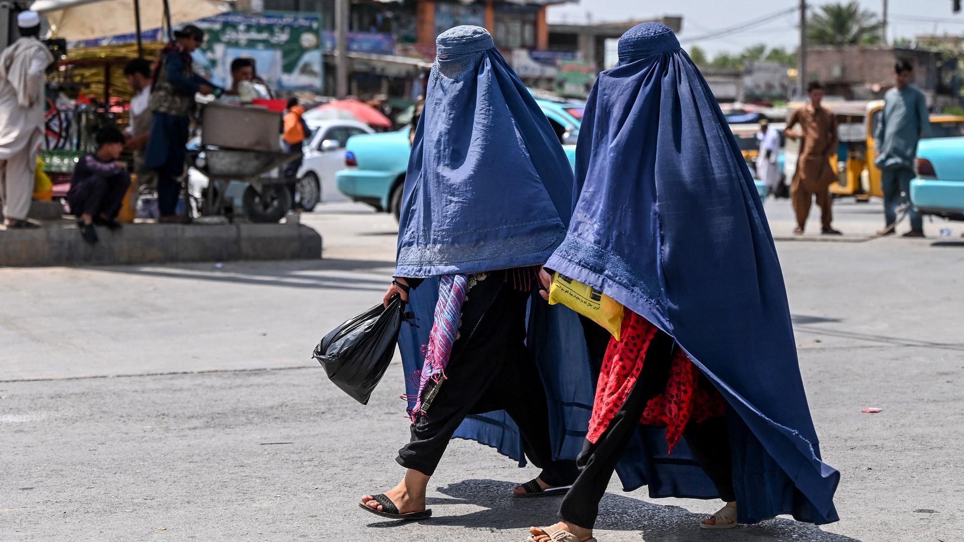 Zwei in eine blaue Burka gehüllte Frauen gehen über eine Straße in Jalalabad, Afghanistan (21.04.2025)