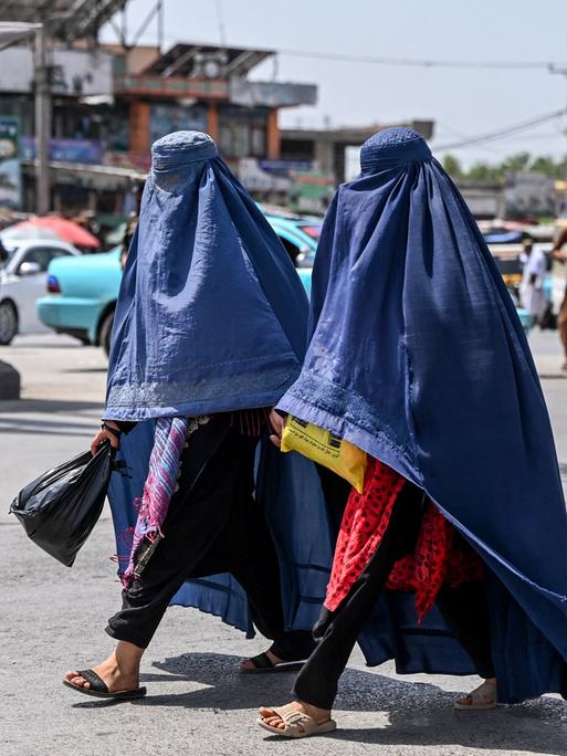 Zwei in eine blaue Burka gehüllte Frauen gehen über eine Straße in Jalalabad, Afghanistan (21.04.2025)