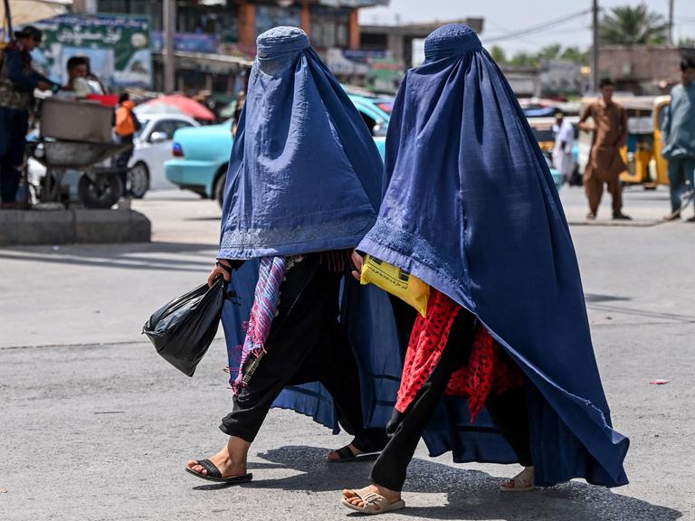 Zwei in eine blaue Burka gehüllte Frauen gehen über eine Straße in Jalalabad, Afghanistan (21.04.2025)