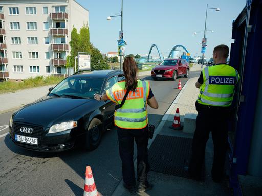 Eine Polizistin und ein Polizist nehmen Grenzkontrollen vor und stoppen dafür Autos.